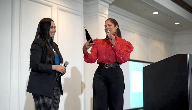 Dos mujeres en un escenario durante un evento de reconocimiento de Transformando Comunidades